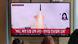 Auf einem großen Bildschirm sind eine startende Rakete und ein koreanischer Schriftzug zu sehen, davor die Hinterköpfe von Menschen, die zuschauen Auf einem großen Bildschirm sind eine startende Rakete und ein koreanischer Schriftzug zu sehen, davor die Hinterköpfe von Menschen, die zuschauen
