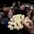 Moldovan President Maia Sandu beams as she is given an enormous bouquet of white roses. She is surrounded by people smiling, clapping and taking photos on their smartphones and a journalist with a television camera