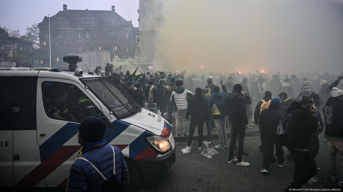 Zahlreiche Personen - Fans von Maccabi Tel Aviv - am Donnerstag vor dem Europa-League-Spiel gegen Ajax auf dem Damplatz in Amsterdam, über ihnen Rauchschwaden, vereinzelt sind Fackellichter zu sehen, im Vordergrund ein Polizeiwagen auf der Straße