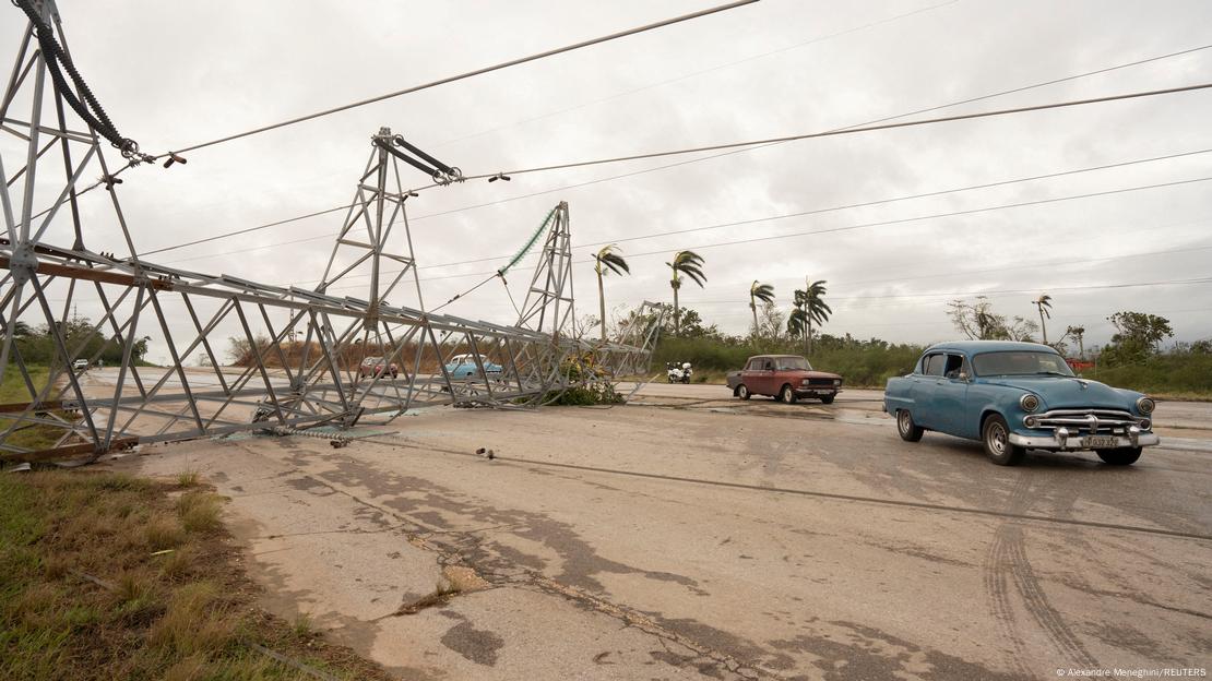 Autos antiguos estadounidenses y soviéticos pasan junto a una torre derribada con cables eléctricos de alta tensión en una carretera, un día después de que el huracán Rafael tocara tierra en Cuba, cerca de Artemisa, Cuba, el 7 de noviembre de 2024.