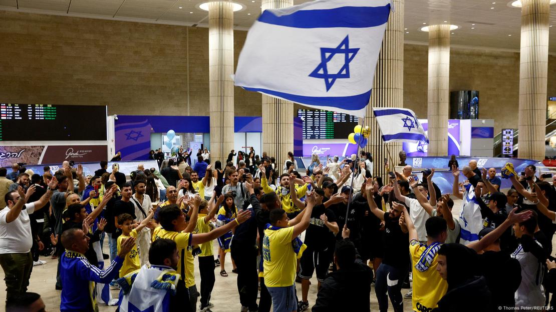 Maccabi-Fans schwenken im Ben-Gurion-Flughafen von Tel Aviv israelische Flaggen und recken die Arme in die Höhe