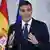 Prime Minister Pedro Sanchez stands in front of a Spanish flag as he speaks to reporters at a press conference