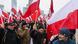A crowd, mostly men, wearing winter coats, hats and rosettes in the Polish national colors and holding up Polish flags take part in a march A crowd, mostly men, wearing winter coats, hats and rosettes in the Polish national colors and holding up Polish flags take part in a march
