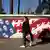 Mulher em Teerã passa por mural que representa bandeira dos Estados Unidos com caveiras no lugar de estrelas e soldados armados