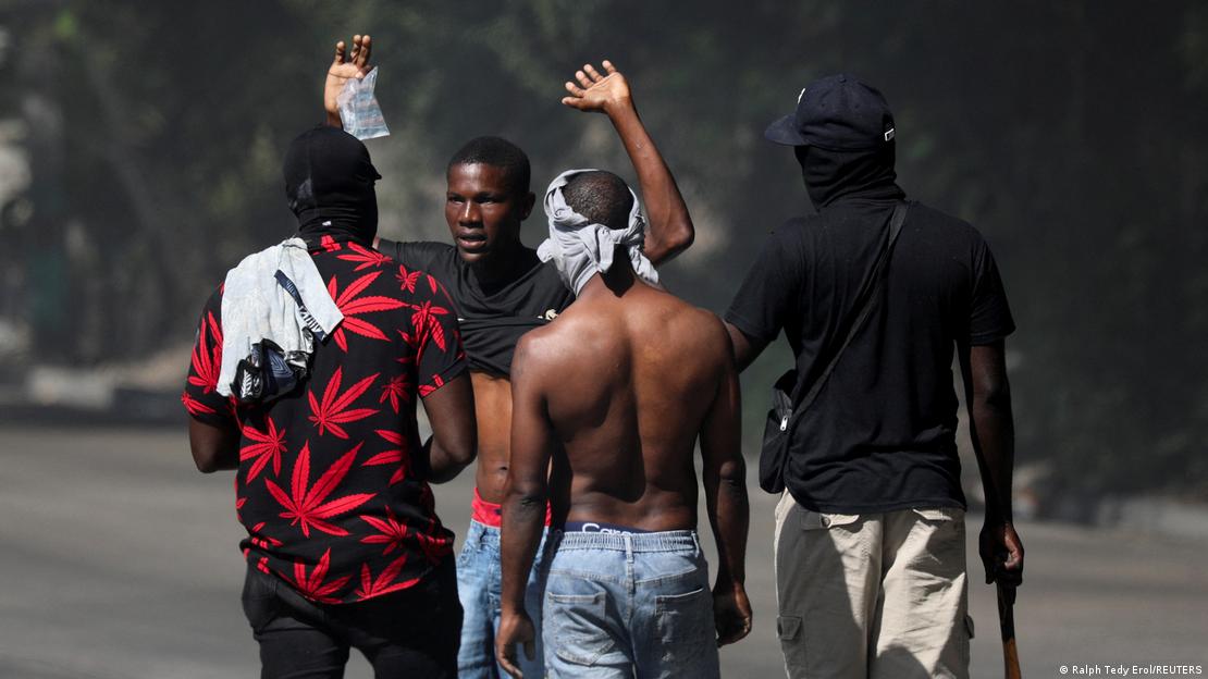 Membros armados de uma gangue interrogam um homem em uma rua