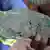 A hand holds a grey and green cobalt rock