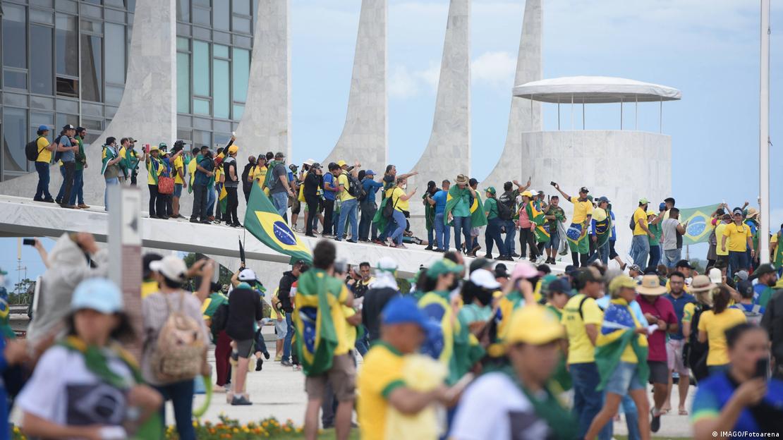 Zahlreiche Menschen stehen vor einem Regierungsgebäude in Brasília und tragen Klamotten in den Nationalfarben (08.01.2023)