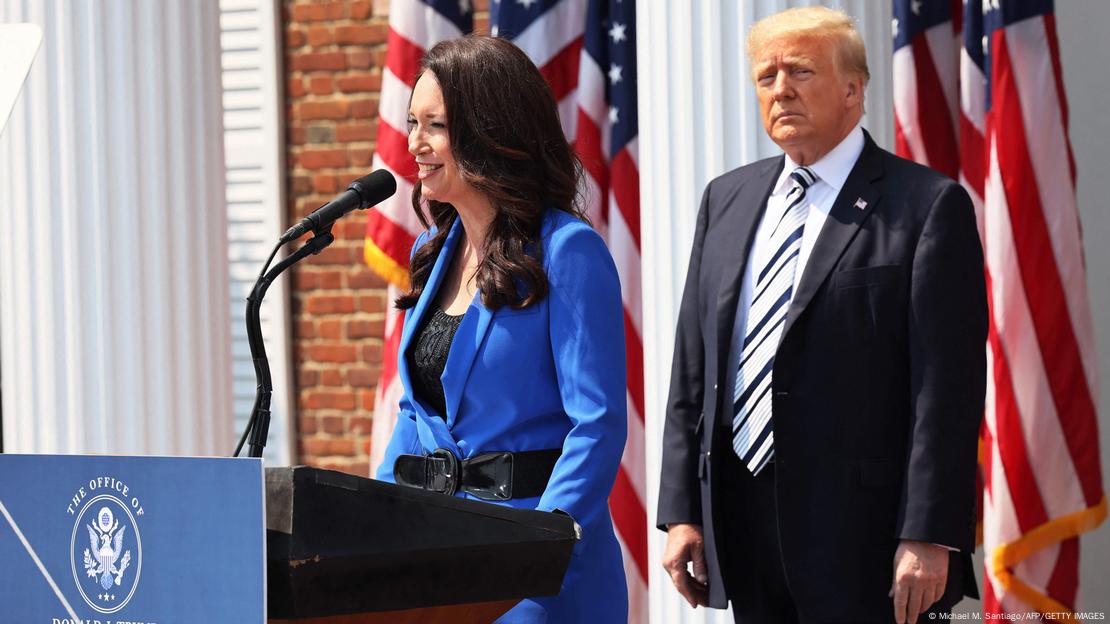 Brooke Rollins steht lächelnd am Mikro während einer Pressekonferenz 2021 in Bedminster in New Jersey. Im Hintergrund steht Donald Trump