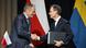 Two men in dark blue suits, in profile, shake hands before their countries' flags: Polish (red and white) and Swedish (blue and yellow) Two men in dark blue suits, in profile, shake hands before their countries' flags: Polish (red and white) and Swedish (blue and yellow)