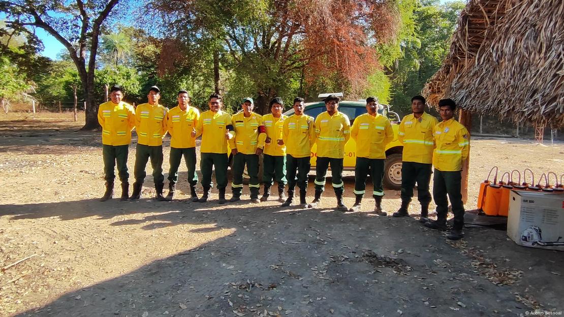 Brigadistas com roupas amarelas enfileirados ao lado de um telhado de palha e diante de uma árvore, na Ilha do Bananal, Tocantins