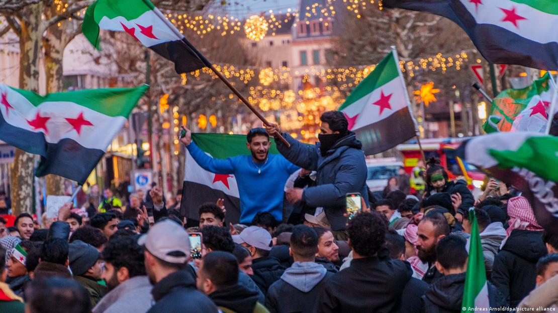 Menschen schwenken syrische Fahnen auf einer Straße mit Weihnachtsbeleuchtung