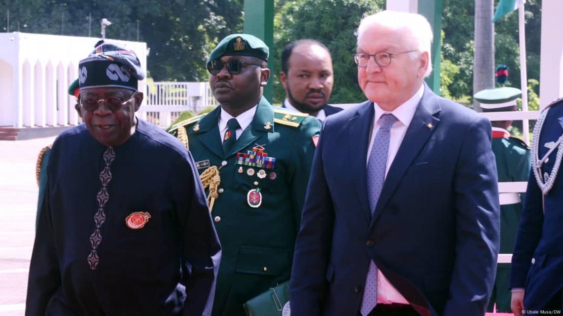 Frank-Walter Steinmeier und Bola Tinubu stehen nebeneinander, im Hintergrund ist ein hochrangiger Militärvertreter zu sehen, der eine Uniform trägt