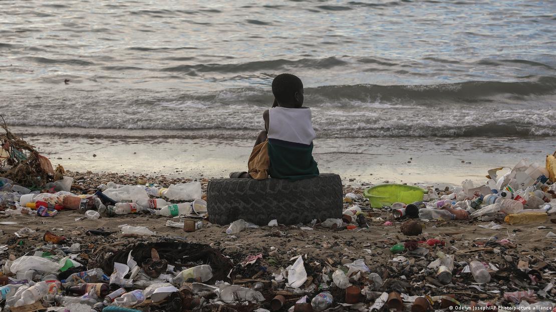 Un chico sentado junto a una playa repleta de basura en Saint Marc, Haití.