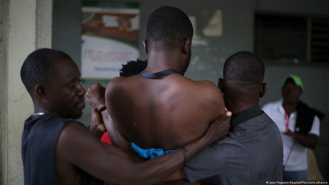 Dos hombres ayudan a un tercero, periodista, herido por un ataque de pandillas a un hospital en Puerto Príncipe, el 24 de diciembre de 2024.