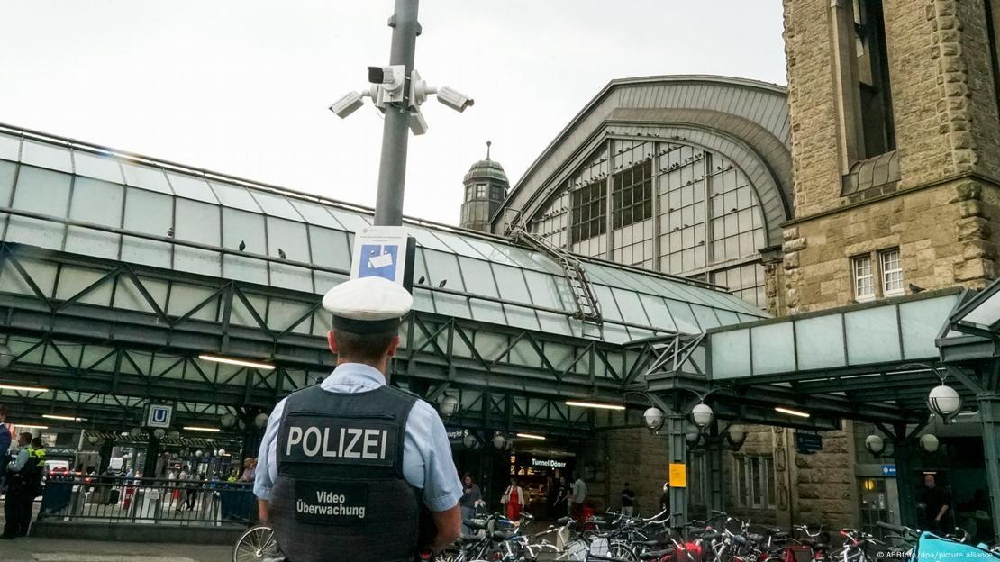 Një polic me kurriz në stacionin e trenit në Hamburg, në një shtyllë shihen kamera sigurie