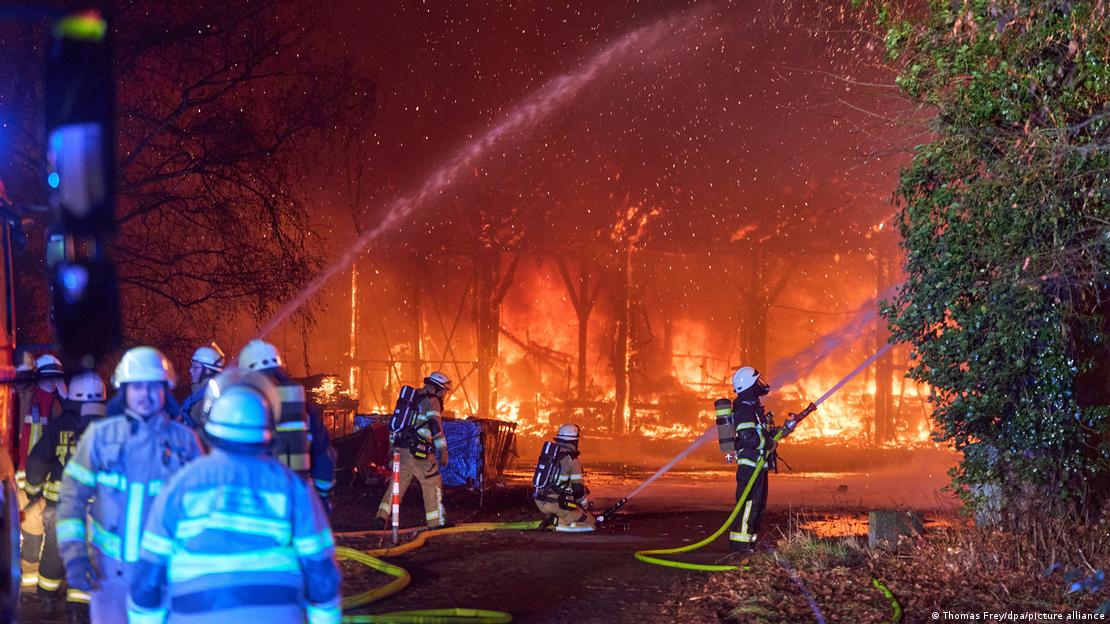 Bombeiros operam mangueiras que jogam água em um armazém em chamas