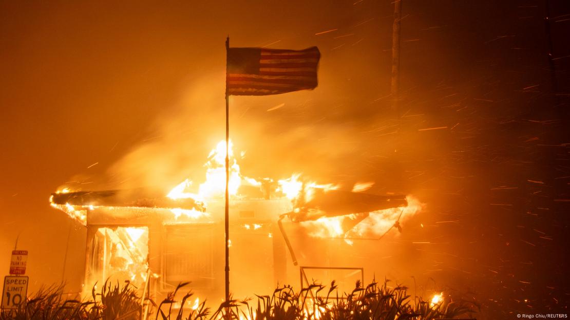Bandeira dos EUA diante de estrutura em chamas em foto noturna Bandeira dos EUA diante de estrutura em chamas em foto noturna