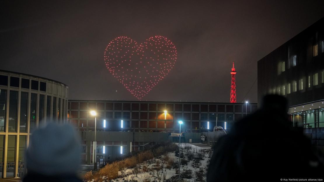 Ein rotes Herz ist in Berlin am Nachthimmel zu sehen, daneben der Berliner Funkturm, ebenfalls rot angeleuchtet. 350 leuchtende Drohnen sind dafür im Einsatz.