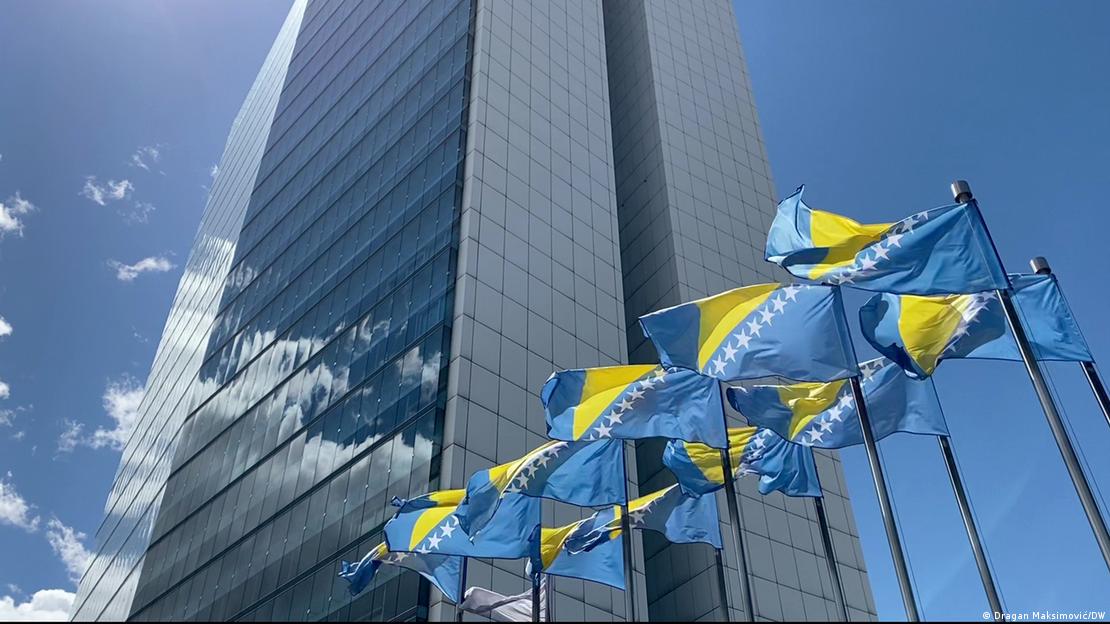 Plava visokokatnica a ispred nje vijore plavo-žute zastave BiH