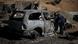 A search and rescue worker investigates the charred remains of a vehicle A search and rescue worker investigates the charred remains of a vehicle