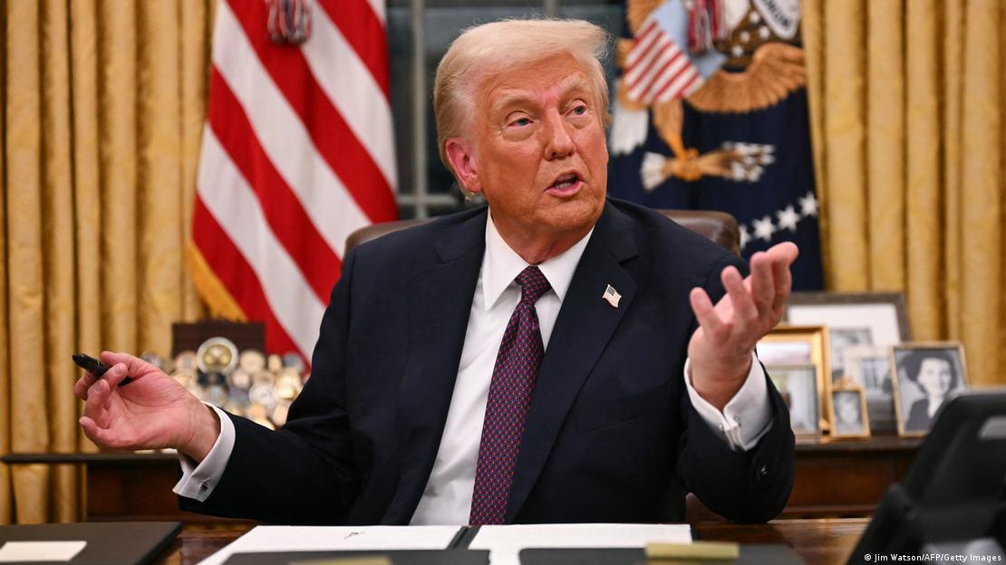 O presidente dos Estados Unidos, Donald Trump, segura uma caneta após assinar um decreto no Salão Oval da Casa Branca. Ele veste terno e gravata escuros, e camisa branca. Ao fundo, está a bandeira dos Estados Unidos e fotos da sua família. O presidente dos Estados Unidos, Donald Trump, segura uma caneta após assinar um decreto no Salão Oval da Casa Branca. Ele veste terno e gravata escuros, e camisa branca. Ao fundo, está a bandeira dos Estados Unidos e fotos da sua família.