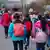 Una hilera doble de escolares de educación primaria camina de espaldas a la cámara, tomados de las manos, de dos en dos.