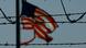 A tattered US flag flying behind barbed wire A tattered US flag flying behind barbed wire