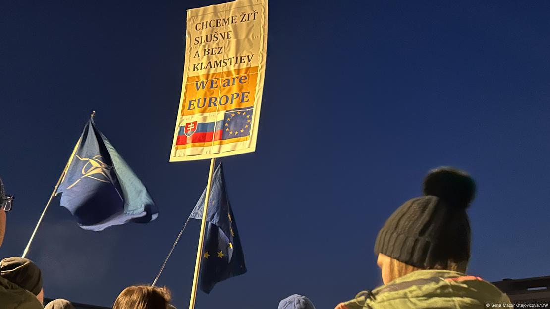 The flags of the EU and NATO and a sign that reads 'We want to live decently and without lies — We are Europe' can be seen above the heads of demonstrators against a darkening sky. Freedom Square, Bratislava, Slovakia, January 24, 2025