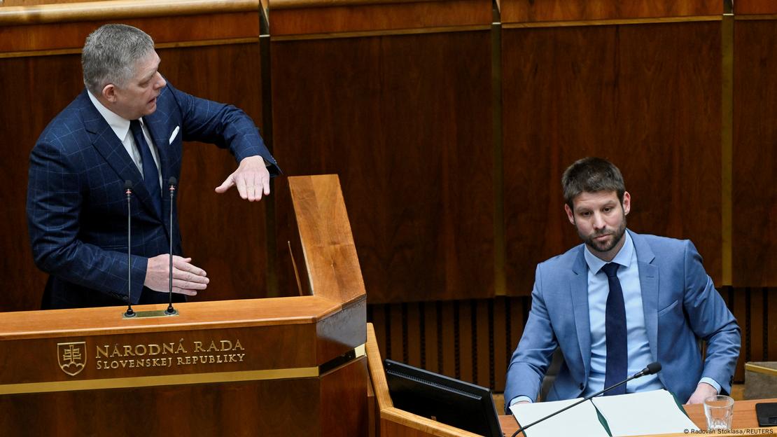 Slovakia's Prime Minister Robert Fico (left) can be seen making large gestures with both hands at the speakers' podium in the Slovak parliament. He is turning to look at Michal Simecka (right), leader of the opposition Progressive Slovakia party leader, who is seated at a desk and looking straight ahead with a very serious expression on his face. Bratislava, Slovakia, January 21, 2025