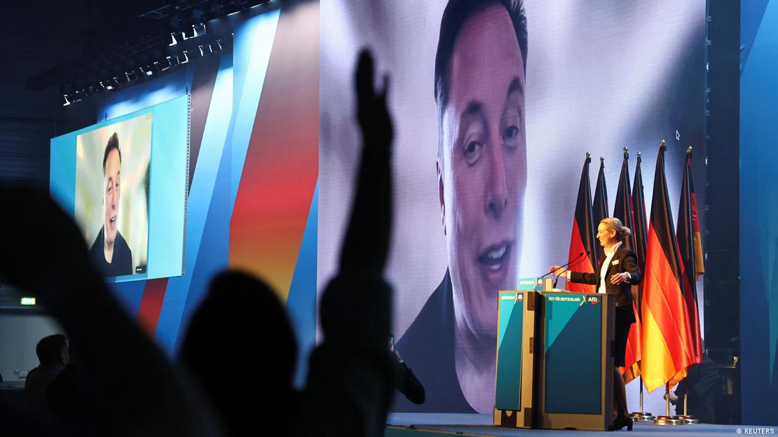 Elon Musk ist beim Wahlkampfauftritt der AfD per Video zugeschaltet und auf einer großen Leinwand hinter Alice Weidel zu sehen, die auf einer Bühne vor Deutschlandflaggen steht