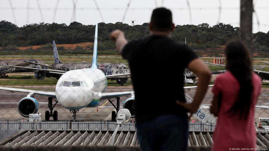 Homem e mulher observam aviões em pista de aeroporto