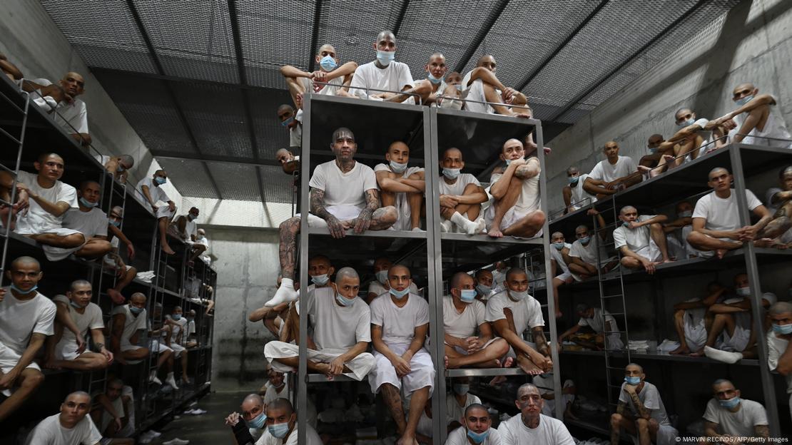 Trajando roupas brancas, detentos posam para foto aglomerados em beliches empilhados numa cela do presídio Cecot, em El Salvador