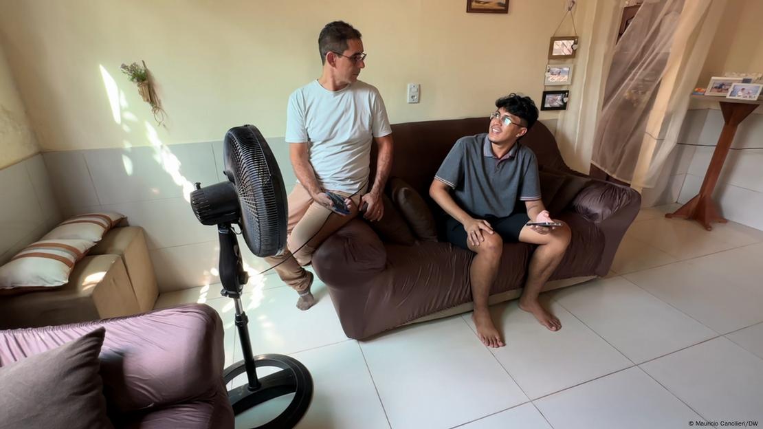 Pai e filho sentandos no sofá da sala da sua casa com o ventilador ligado para alivar o calor