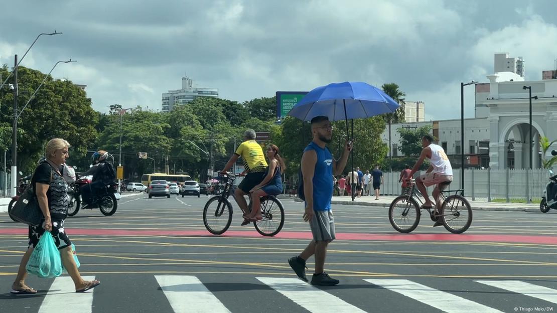 Homem atravessa a rua segurando uma sombrinha para se proteger do sol