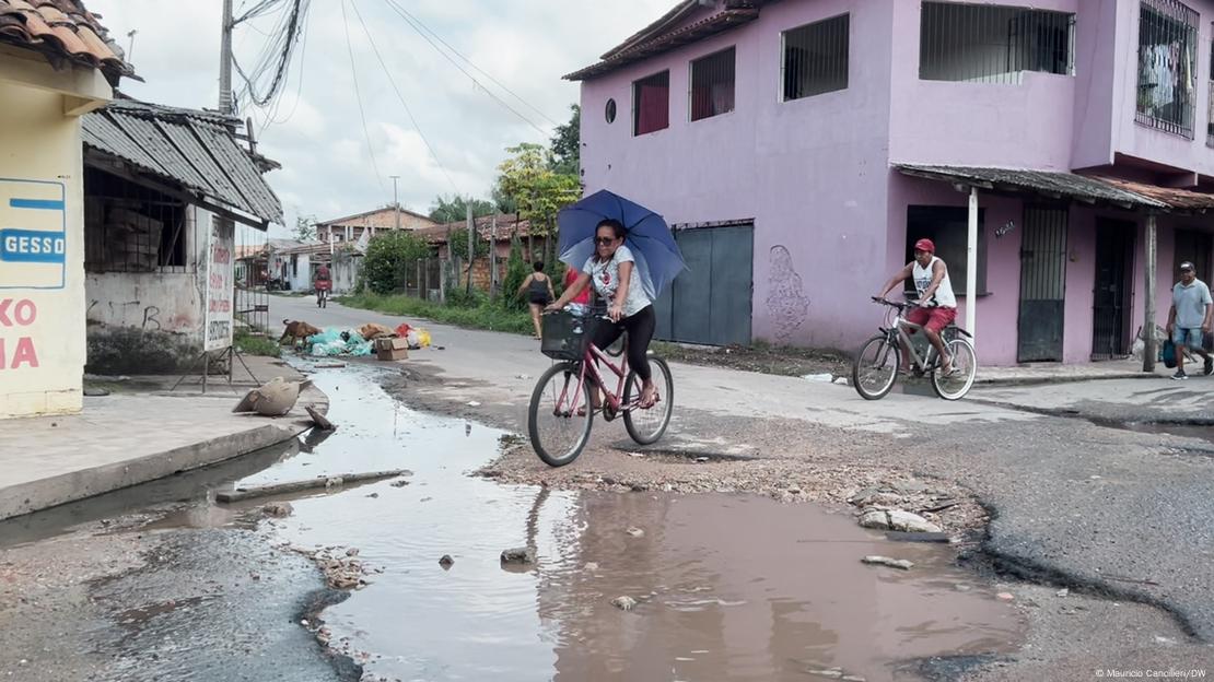 Mulher segura sombrinha enquanto pedala sua bicicleta num bairro da periferia dos arredores Belém