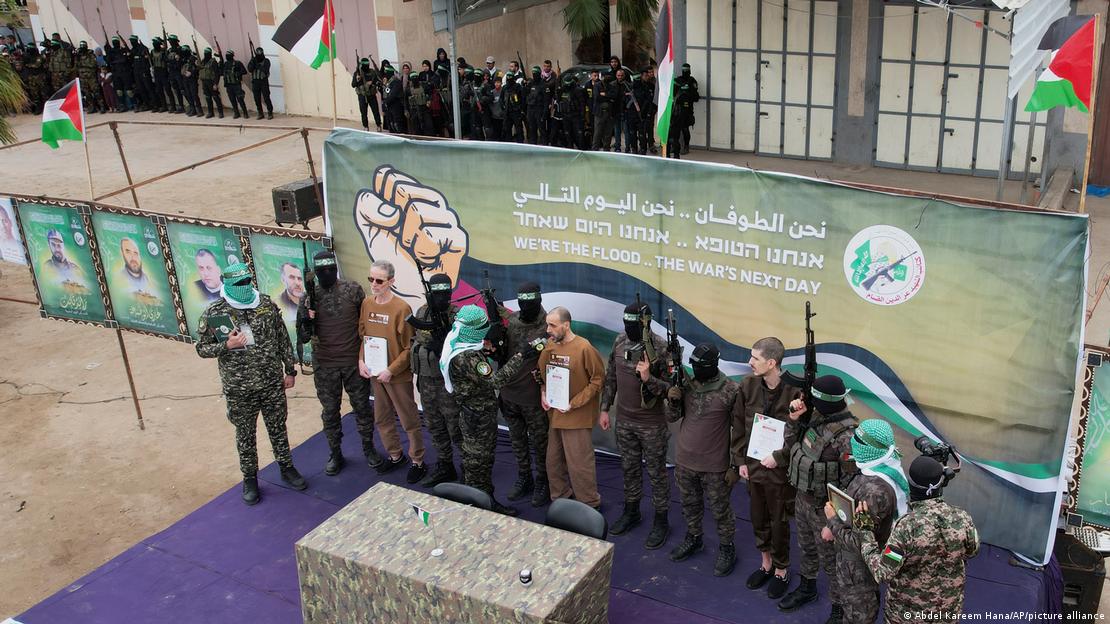 Reféns são exibidos em um palco por militantes uniformizados e encapuzados do Hamas Reféns são exibidos em um palco por militantes uniformizados e encapuzados do Hamas