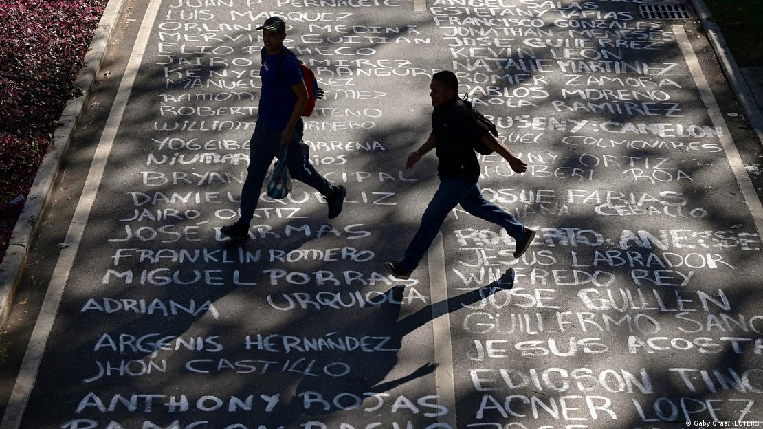 Dos personas cruzando una calle con los nombres escritos de estudiantes asesinados.