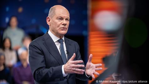 Olaf Scholz duke folur me gjestikulim në një studio televizive, në sfond është publiku