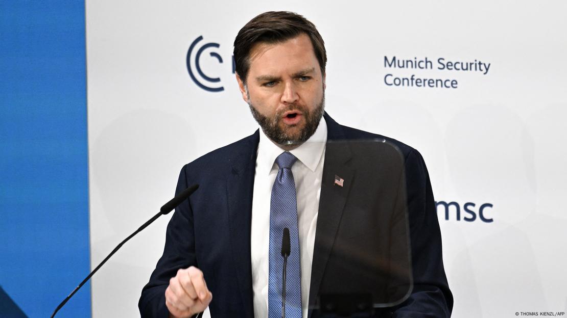 J.D. Vance discursando em palco, com inscrição ao fundo: °Munich Security Conference"