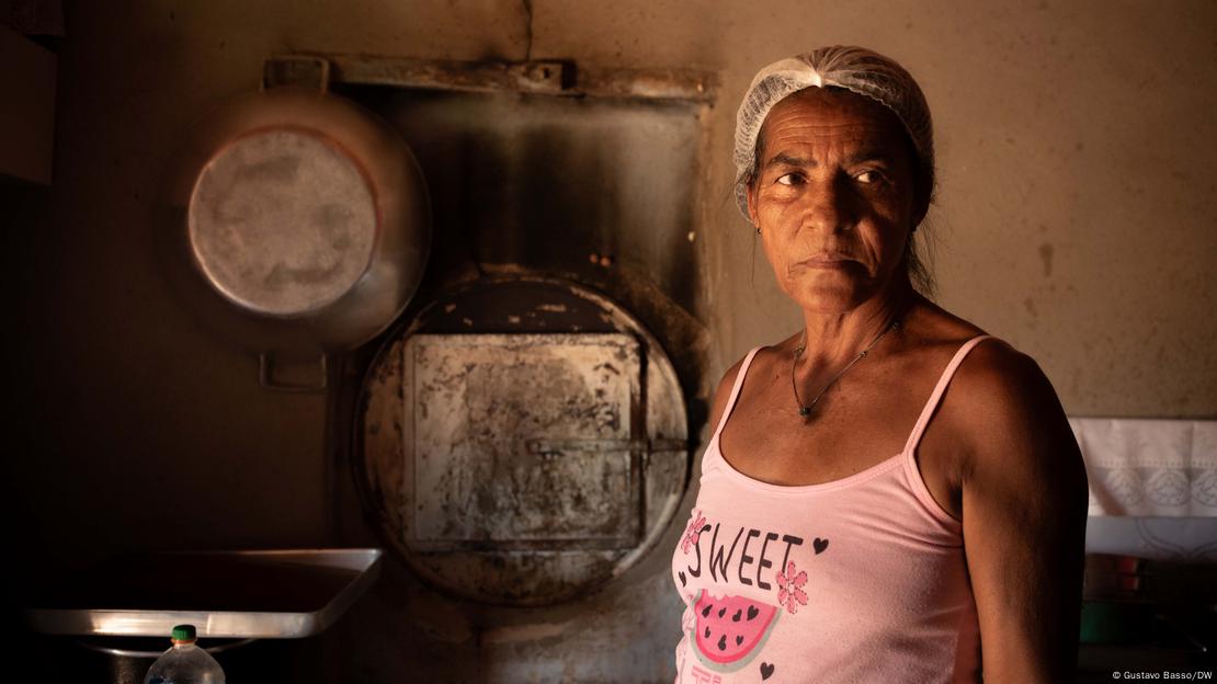 Mulher usando regata rosa e com rede cobrindo os cabelos, diante de forno com porta de metal