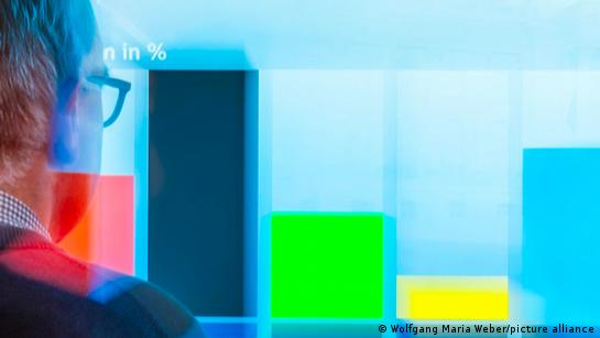 Un uomo guarda un grafico su uno schermo gigante che mostra i risultati per SPD, CDU, Verdi, FDP e AfD.
