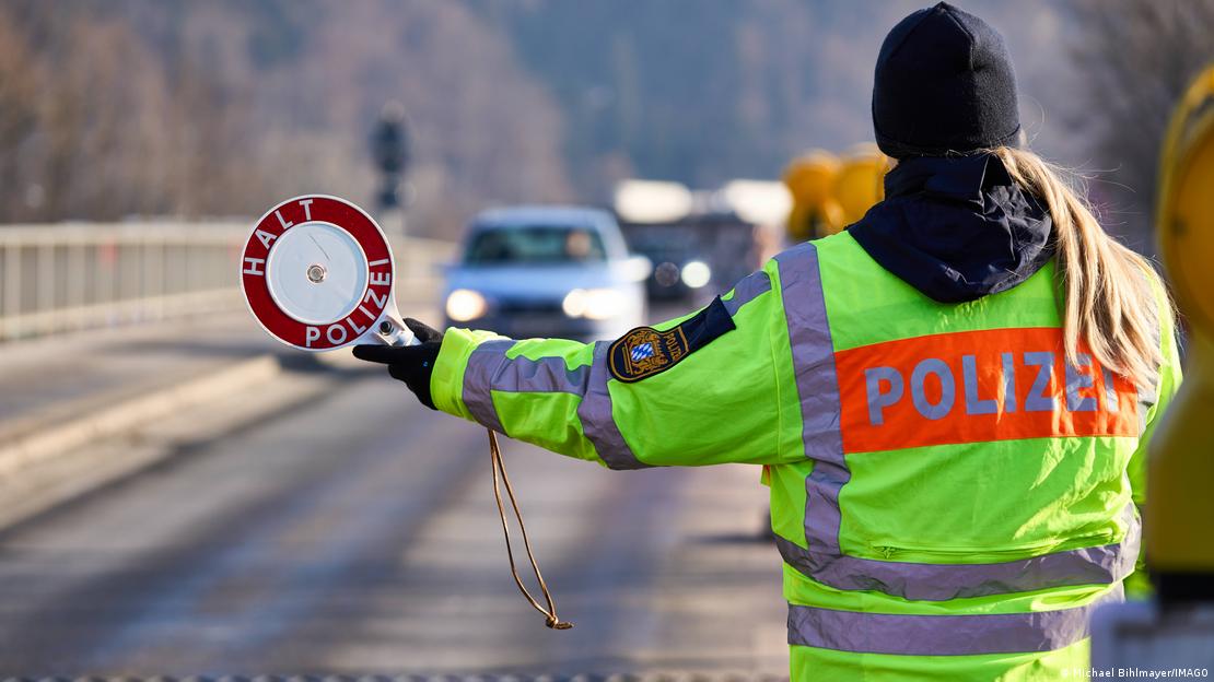 Polizist hält an einer Straße eine Kelle mit der Aufschrift "Halt Polizei" hoch