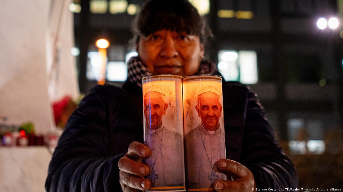 Un fiel boliviano sostiene dos velas con la imagen de Francisco.