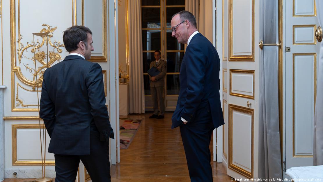 Friedrich Merz und Emmanuel Macron stehen vor einer geöffneten Tür und schauen sich an