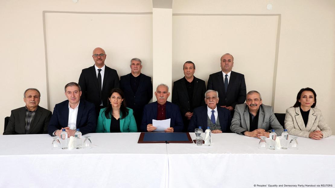DEM Parti heyeti İmralı'da Abdullah Öcalan'la bir masada yan yana oturuyor, Öcalan ortada elinde ilk açıklamasına ilişkin bir kağıt tutuyor 