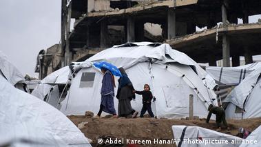 A Palestinian family walk between tents in a sprawling tent camp adjacent to destroyed homes and buildings in Gaza City.