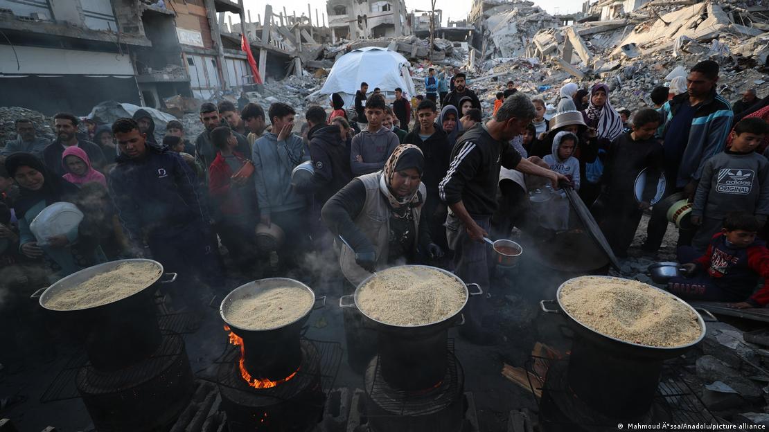 Pessoas fazem fila em frente a panelões de comida em meio a edifícios destruídos em Gaza