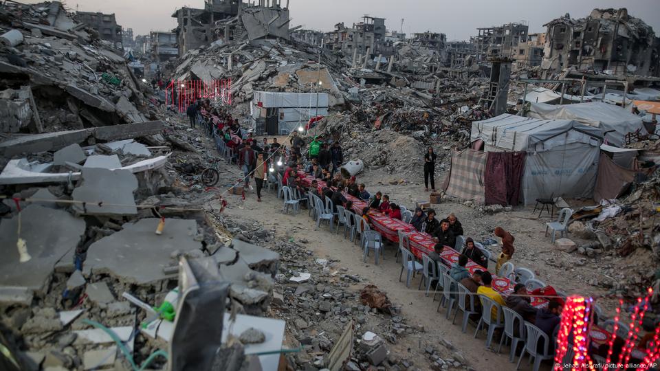 Personas sentadas a una mesa larga en la ciudad de Yabalia, en la Franja de Gaza, entre las ruinas, durante la cena luego del ayuno de Ramadán (6.03.2025). Personas sentadas a una mesa larga en la ciudad de Yabalia, en la Franja de Gaza, entre las ruinas, durante la cena luego del ayuno de Ramadán (6.03.2025).