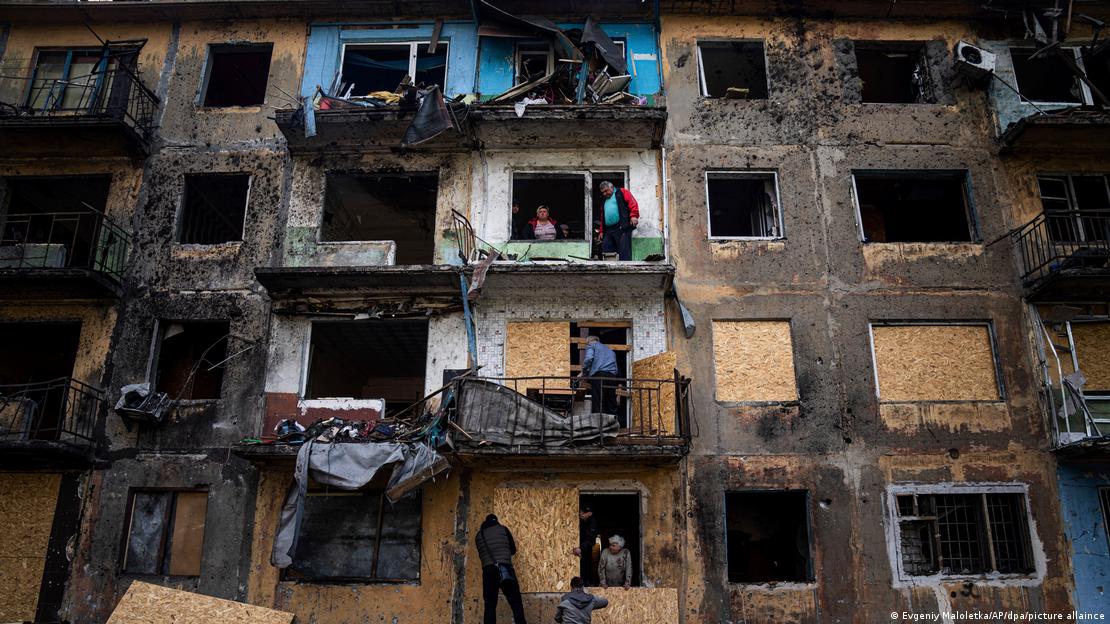 Prédio danificado após bombardeio, com pessoas reparando janelas