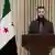 Ahmed al-Scharaa im März bei einer Ansprache an die Nation am Rednerpult, neben einer syrischen Flagge
